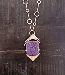 Pendentif artisanal en argent et pierre de charoite violette sur une chaîne à maillons fins.