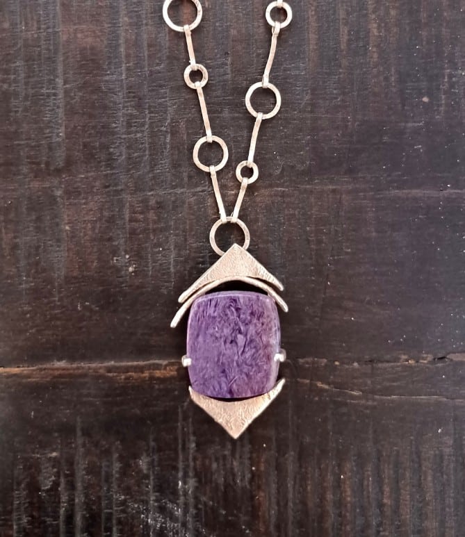 Pendentif artisanal en argent et pierre de charoite violette sur une chaîne à maillons fins.