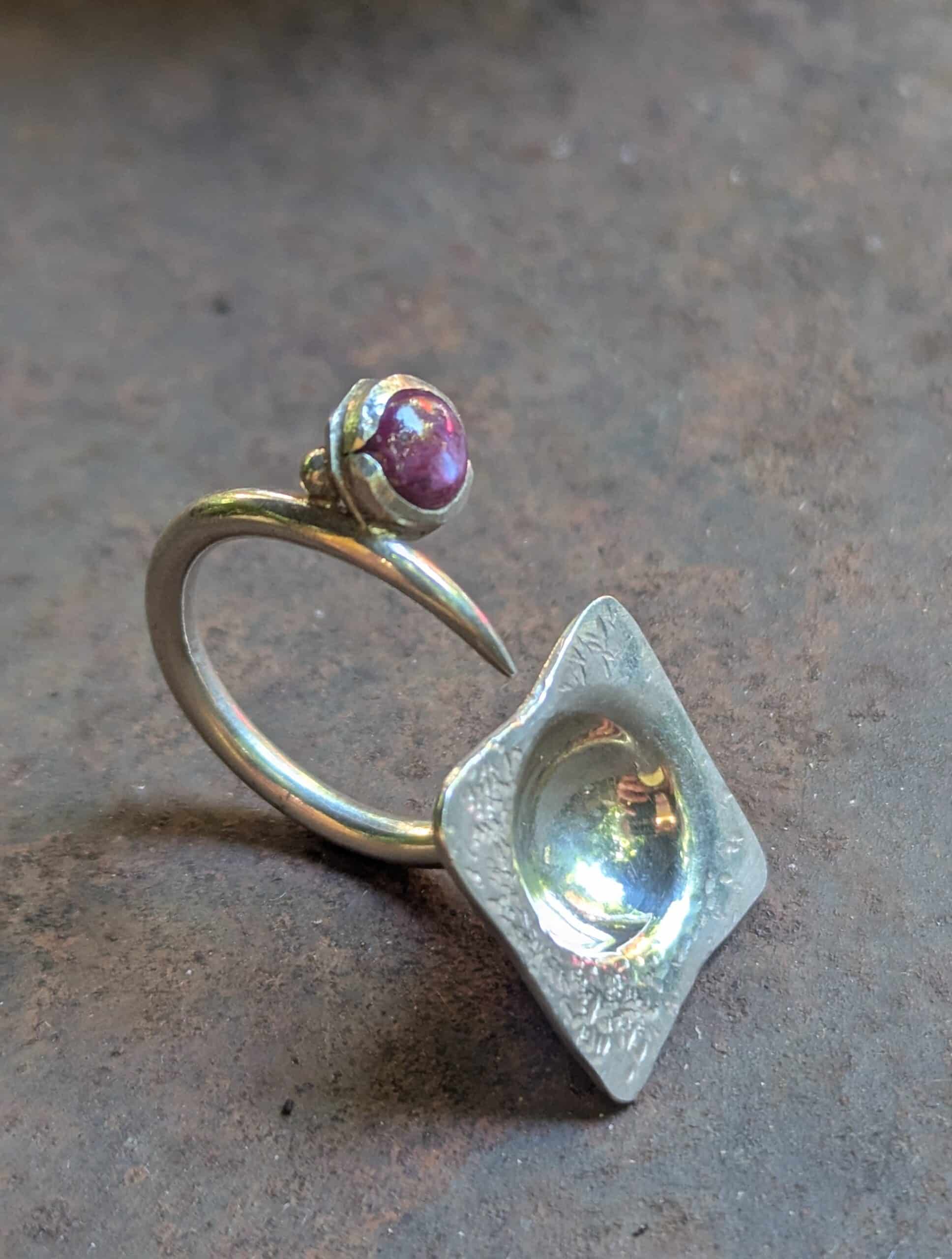 Bague en Argent Artisanale avec Rubis et Design Carré Bague artisanale en argent à anneau ouvert, ornée d'un rubis et d'un élément carré concave texturé.