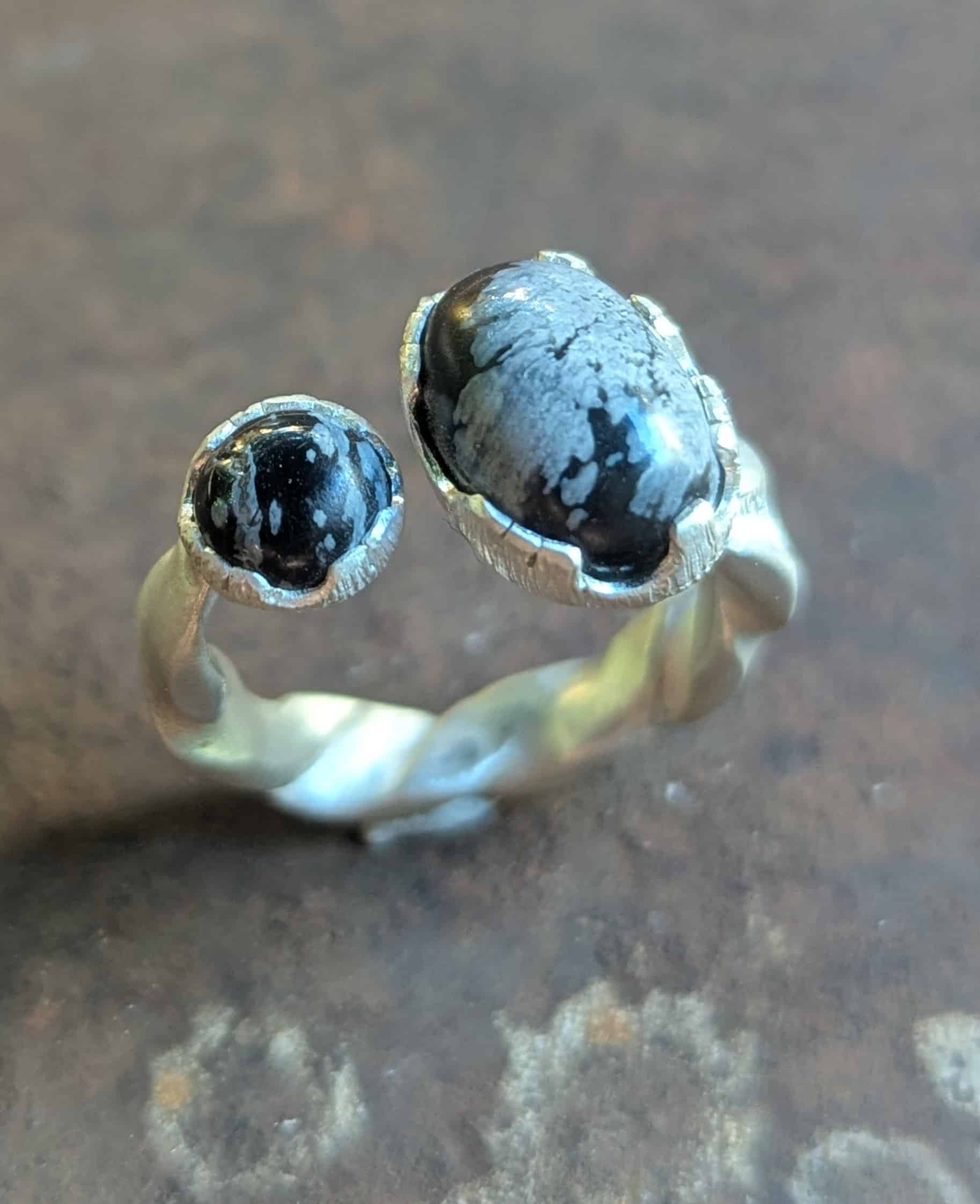 Bague Toi et Moi en Argent et Obsidienne Flocon de Neige Bague toi et moi en argent brossé avec deux obsidiennes flocon de neige, anneau torsadé au style artisanal.